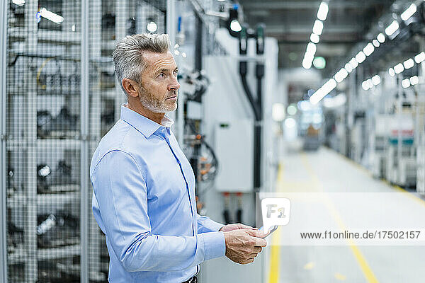 Businessman holding tablet PC contemplating at factory
