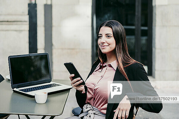 Young businesswoman with laptop and mobile phone at sidewalk cafe