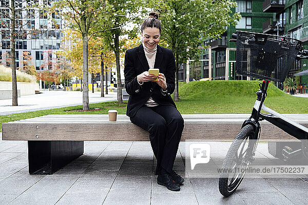 Smiling businesswoman using smart phone sitting on bench
