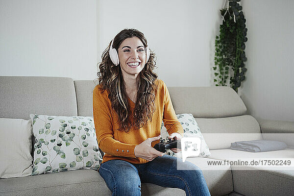 Glückliche Frau mit Kopfhörern  die zu Hause ein Spiel über den Joystick spielt