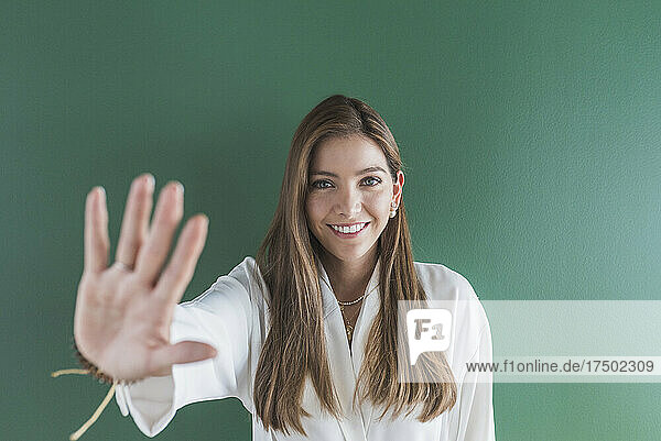 Lächelnde Frau zeigt Stoppschild vor grünem Hintergrund