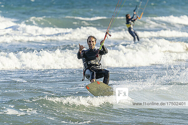 Smiling man kiteboarding with woman in background on vacation