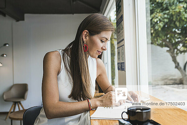 Frau schreibt Tagebuch und sitzt im Café