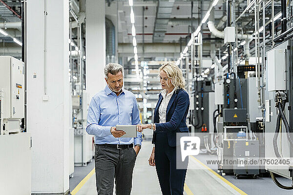 Businesswoman explaining colleague over tablet PC in factory