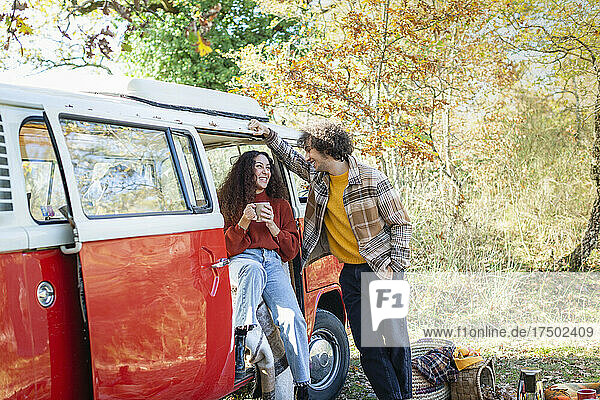 Smiling man leaning on van talking with woman at campervan