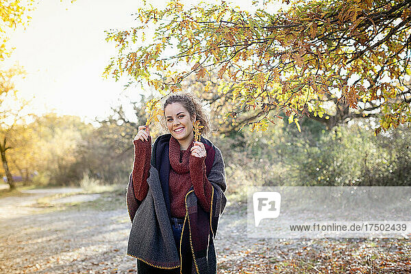 Smiling beautiful woman holding autumn leaves in forest on weekend