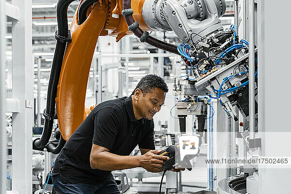 Maintenance engineer operating robot arm in electrical factory