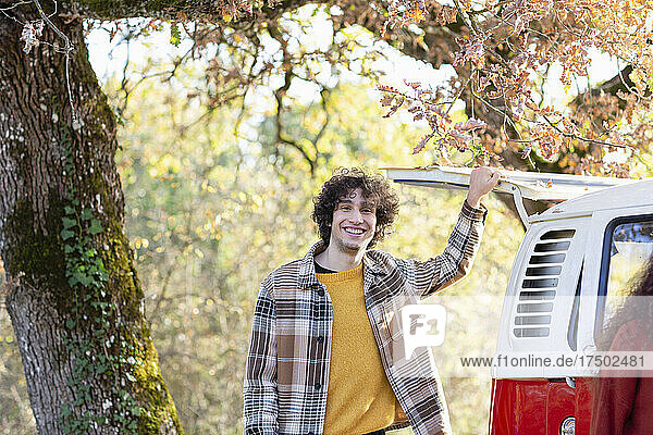 Smiling young man standing at campervan