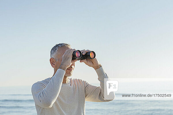 Man looking through binoculars at beach
