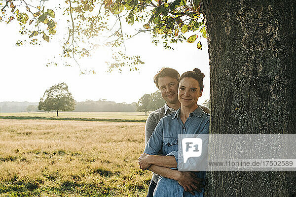 Couple standing by tree in park on sunny day