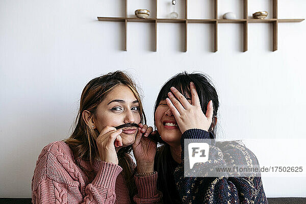 Smiling woman covering face with hand by friend making mustache from her hair