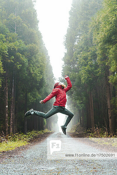 Carefree man jumping on road amidst trees