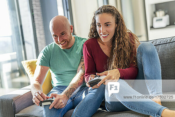 Smiling couple with video game controller playing on sofa