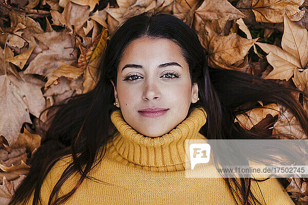 Young woman wearing sweater lying on dry autumn leaf