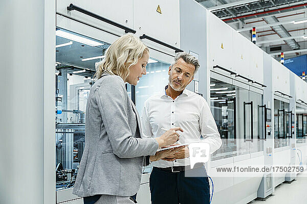 Businesswoman explaining colleague over tablet PC at modern factory