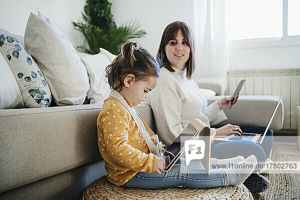 Frau betrachtet kleines Mädchen mit Tablet-PC im Wohnzimmer