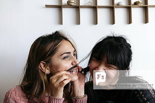 Smiling woman playing with friend hair at home