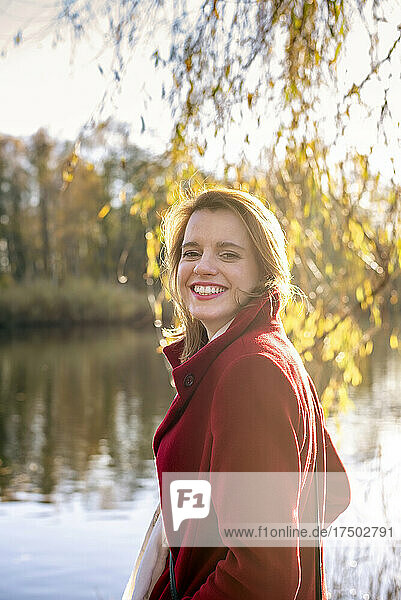 Smiling woman with jacket standing at lakeside