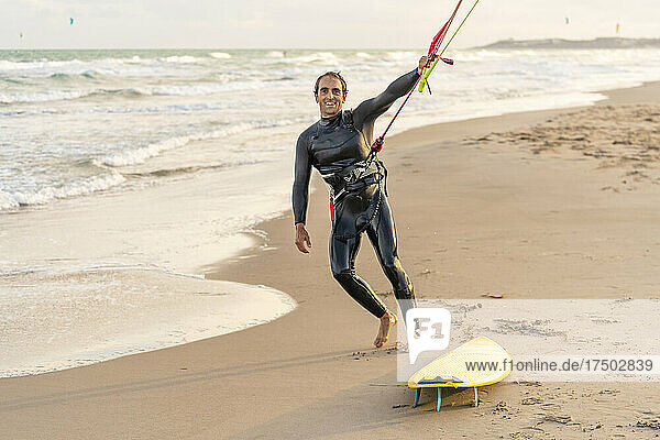 Smiling man holding rope of parachute by kiteboard at beach