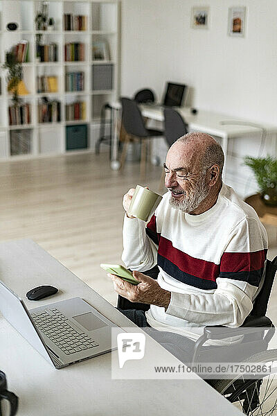 Businessman with mobile phone having coffee at home office