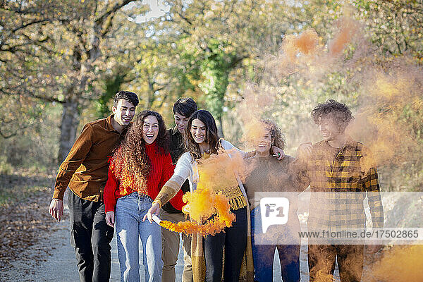 Cheerful woman enjoying smoke flare with friends in autumn forest
