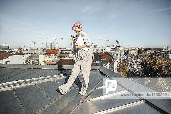 Woman with laptop and headphones standing on rooftop