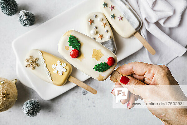 Woman's hand holding Christmas cake pop over plate