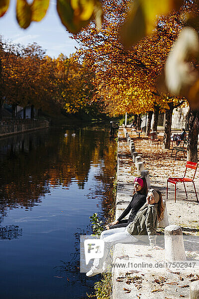 Teenage friends sitting at canal on sunny day