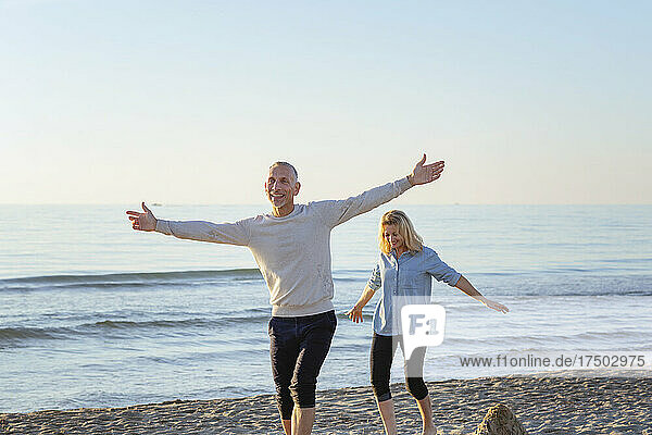 Carefree couple playing with arms outstretched at beach