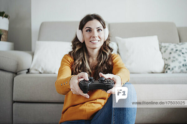 Junge Frau mit Kopfhörern spielt zu Hause Videospiel