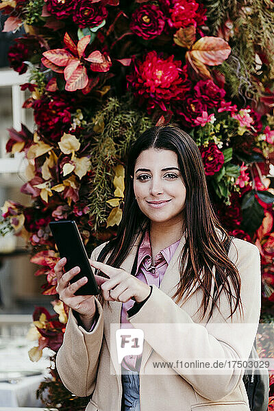 Young businesswoman holding mobile phone in front of flowers