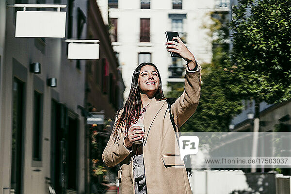 Lächelnde Geschäftsfrau  die an einem sonnigen Tag ein Selfie mit dem Smartphone macht