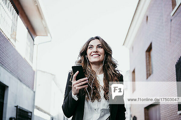 Smiling businesswoman listening music on smart phone