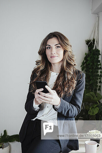 Geschäftsfrau mit braunen Haaren hält Smartphone im Büro