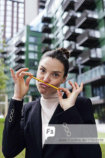 Businesswoman making mustache with pencil on puckered lips at office park