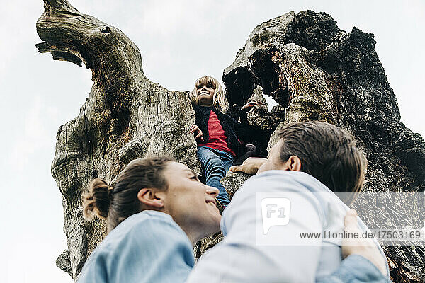 Smiling girl standing on tree trunk with parents in park