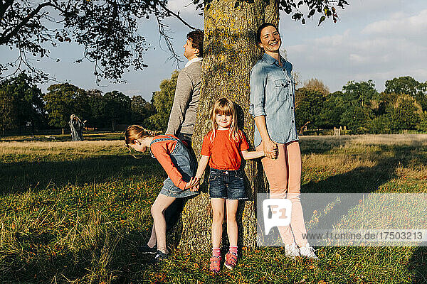 Family holding hands standing around tree in park