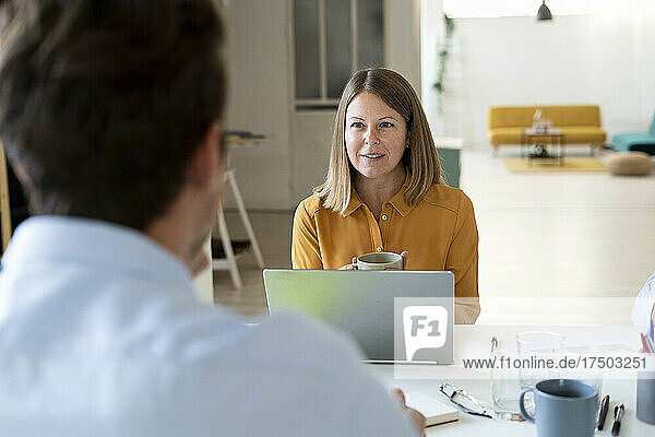 Businesswoman with cup looking at colleague in office