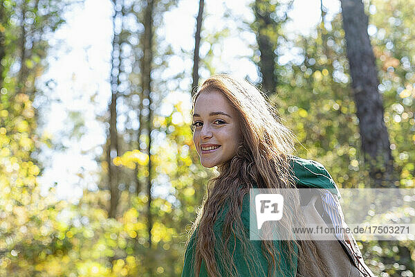 Smiling woman with backpack in forest on sunny day