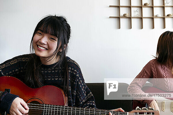 Smiling woman playing guitar with friend at home
