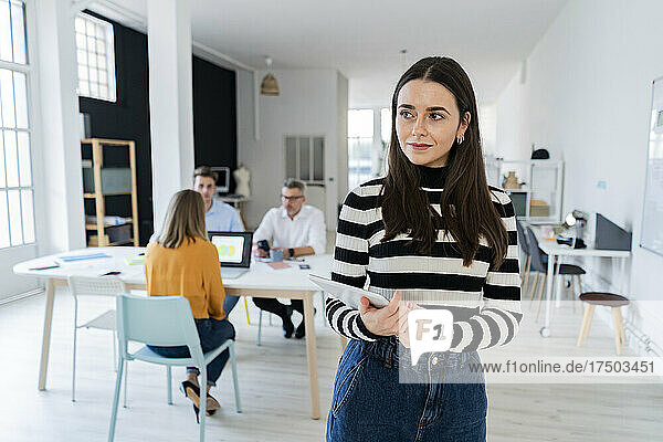 Contemplative businesswoman with tablet PC standing in modern office