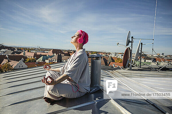 Woman with headphones meditating on rooftop