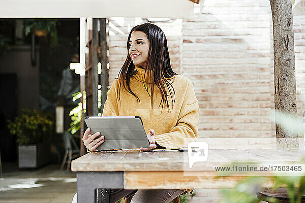 Lächelnde Frau mit digitalem Tablet sitzt im Straßencafé