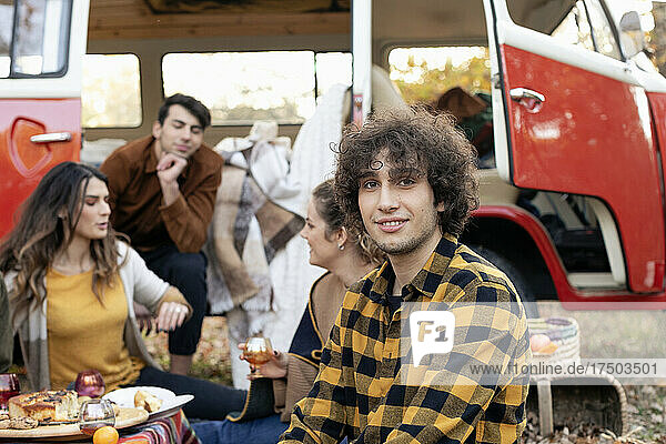 Smiling man with friends talking outside van on picnic