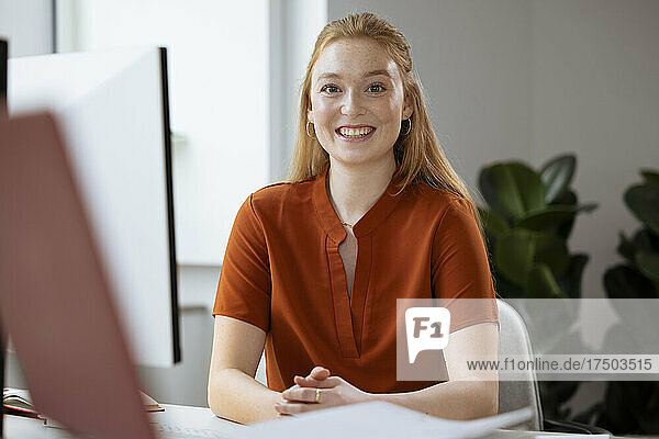 Lächelnde junge Geschäftsfrau  die am Schreibtisch sitzt