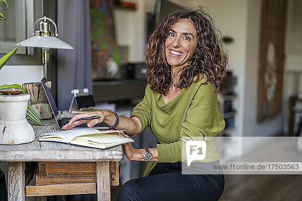 Smiling woman with diary and laptop at table