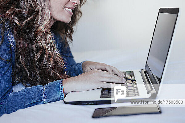 Smiling young woman using laptop in bedroom