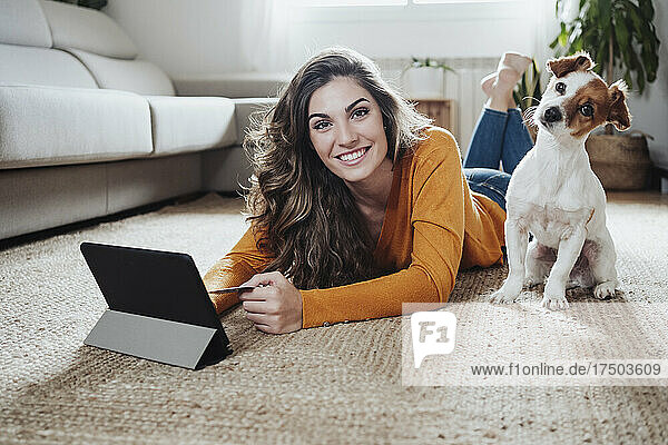 Woman with tablet PC lying on floor with dog at home