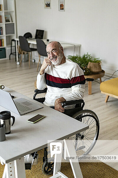 Lächelnder älterer Geschäftsmann sitzt im Rollstuhl im Heimbüro