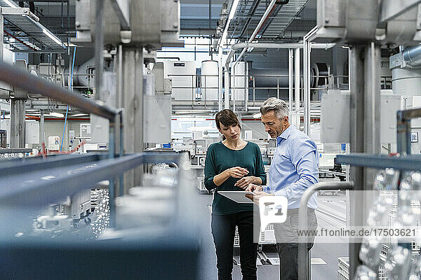 Businesswoman discussing over tablet PC with coworker at factory